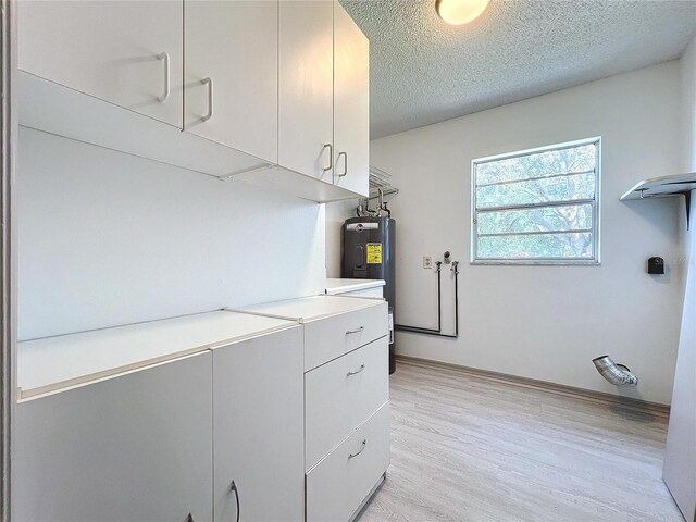 laundry room featuring water heater, light hardwood / wood-style floors, and a textured ceiling