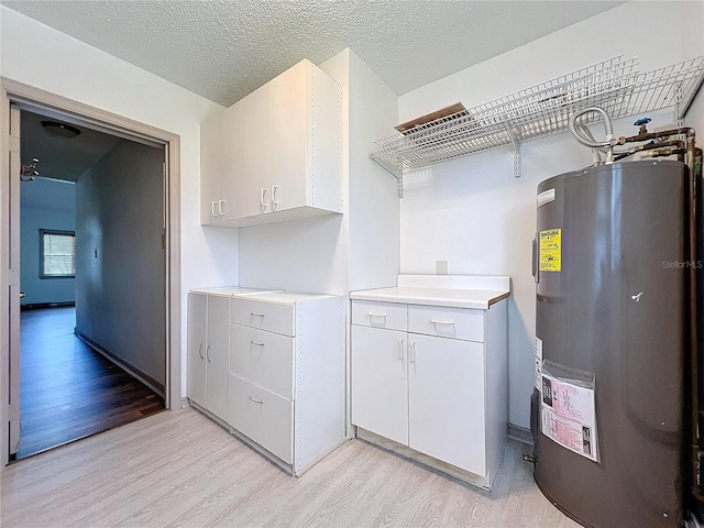 clothes washing area with a textured ceiling, electric water heater, and light hardwood / wood-style floors