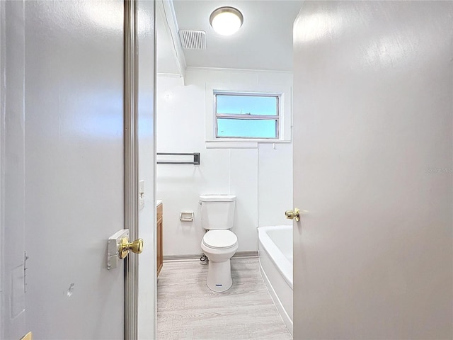 bathroom with a tub, hardwood / wood-style floors, vanity, and toilet