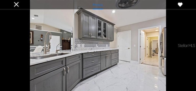 kitchen with lofted ceiling, sink, gray cabinetry, stainless steel refrigerator, and light stone countertops