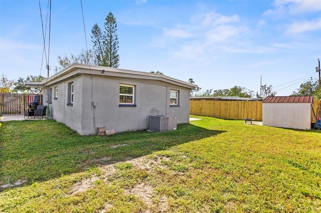 back of house featuring central air condition unit, a yard, and a storage shed