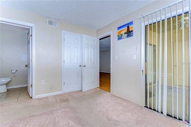 unfurnished bedroom featuring ensuite bathroom, a closet, light colored carpet, and a textured ceiling