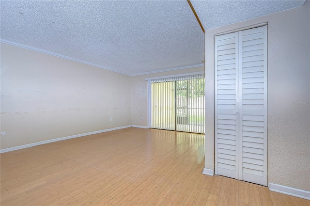 interior space with a textured ceiling, light wood-type flooring, ornamental molding, and a closet