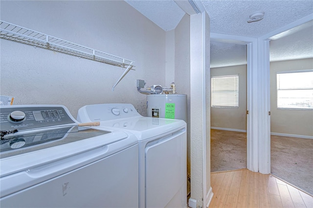 clothes washing area featuring washer and clothes dryer, water heater, a textured ceiling, and light hardwood / wood-style flooring