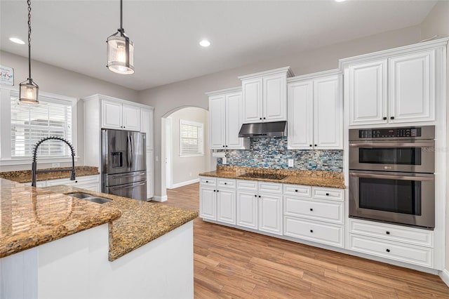 kitchen with stainless steel appliances, sink, decorative light fixtures, white cabinets, and light hardwood / wood-style floors