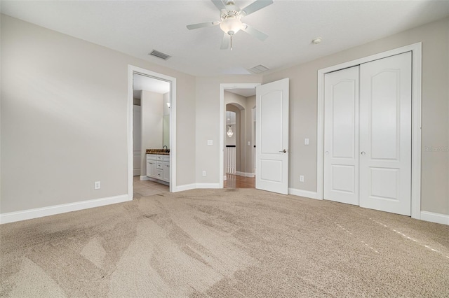 unfurnished bedroom featuring ceiling fan, ensuite bath, light carpet, and a closet