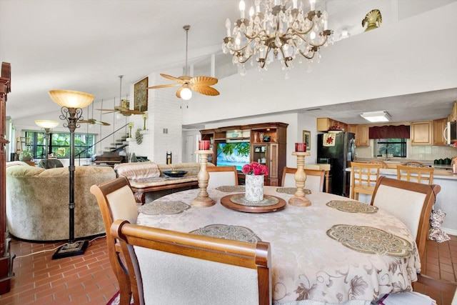 dining area with brick floor, stairway, high vaulted ceiling, and ceiling fan with notable chandelier