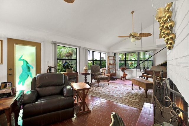 living area featuring brick floor, a lit fireplace, high vaulted ceiling, and ceiling fan