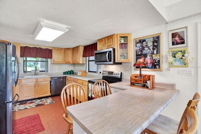 kitchen featuring glass insert cabinets, appliances with stainless steel finishes, a peninsula, light countertops, and a sink