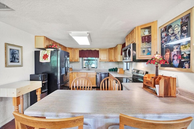 kitchen with stainless steel appliances, light countertops, glass insert cabinets, a sink, and a textured ceiling