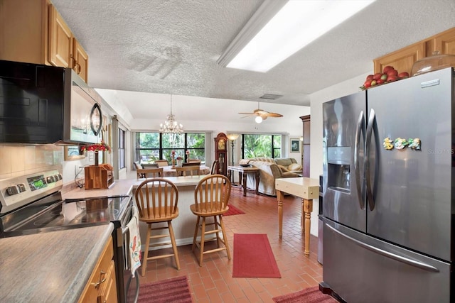 kitchen featuring brick floor, a peninsula, open floor plan, appliances with stainless steel finishes, and tasteful backsplash