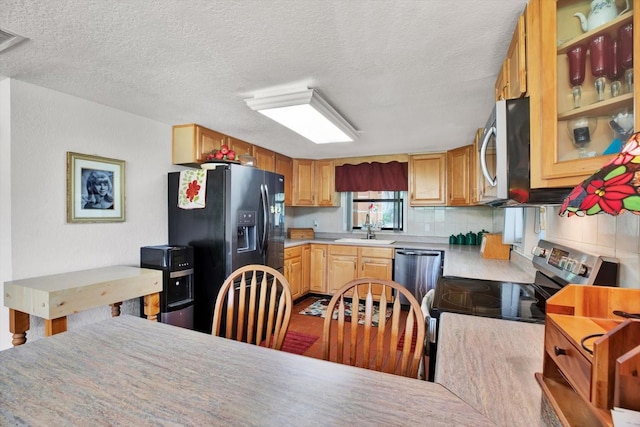 kitchen with light countertops, backsplash, appliances with stainless steel finishes, glass insert cabinets, and a sink