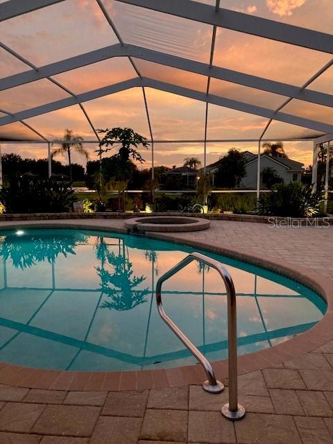 pool at dusk with glass enclosure and a patio