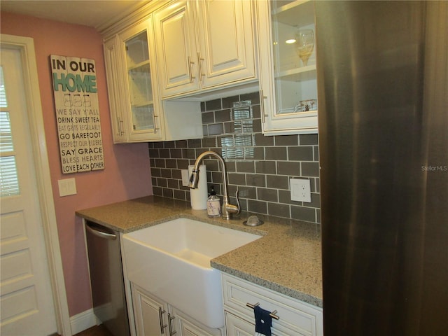 kitchen featuring white cabinetry, sink, light stone countertops, stainless steel dishwasher, and decorative backsplash