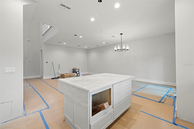 kitchen with white cabinetry, light stone countertops, decorative light fixtures, a notable chandelier, and a center island