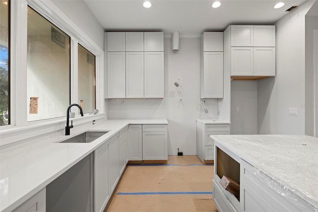 kitchen featuring white cabinetry, sink, and light stone counters