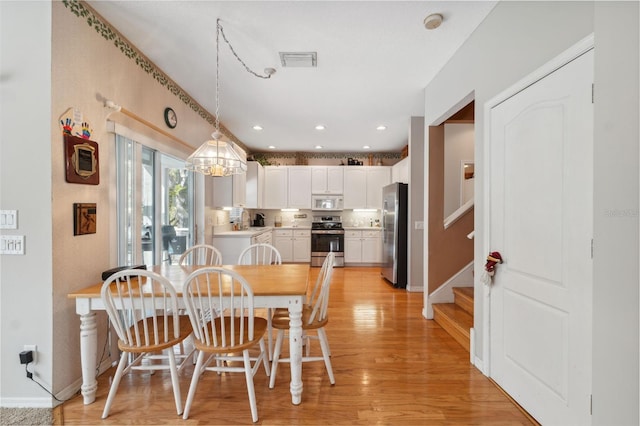 dining space with light wood-type flooring, an inviting chandelier, and sink