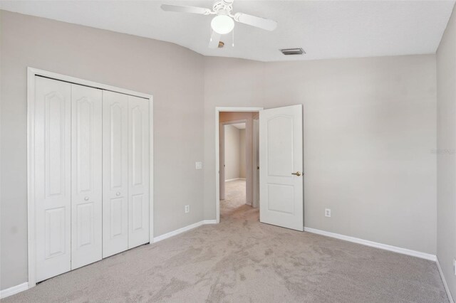 unfurnished bedroom with light colored carpet, a closet, lofted ceiling, and ceiling fan