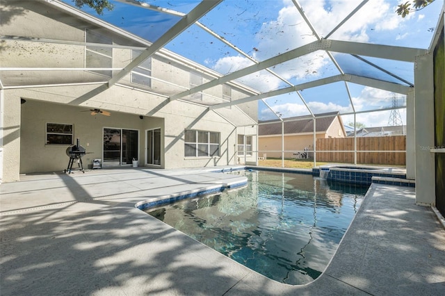 view of pool with an in ground hot tub, a patio, glass enclosure, and ceiling fan