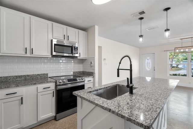 kitchen featuring appliances with stainless steel finishes, decorative light fixtures, white cabinetry, sink, and a kitchen island with sink