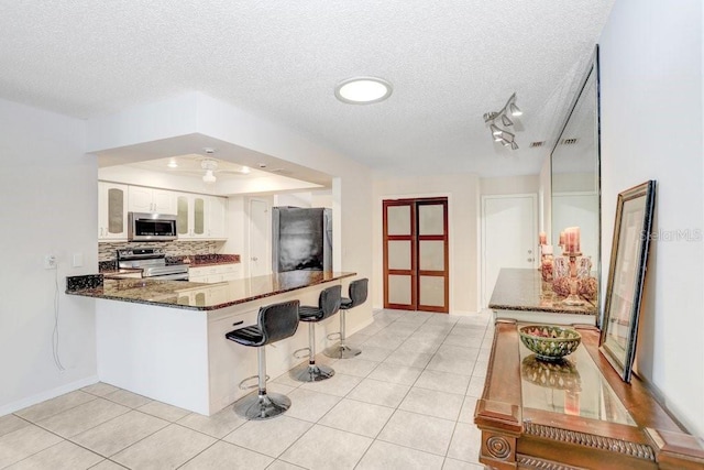 kitchen with kitchen peninsula, dark stone countertops, a textured ceiling, appliances with stainless steel finishes, and white cabinetry