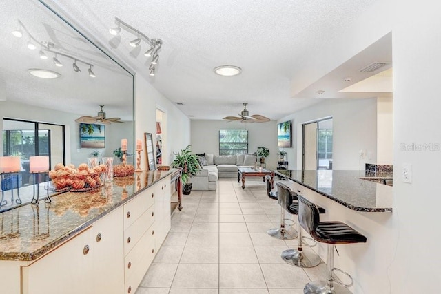 kitchen with plenty of natural light, light tile patterned floors, dark stone counters, and a textured ceiling