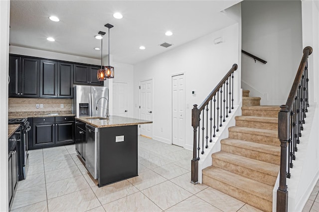 kitchen featuring pendant lighting, a center island with sink, sink, light stone countertops, and stainless steel appliances