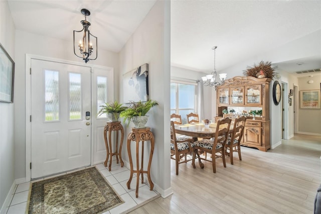 foyer entrance with light hardwood / wood-style floors, vaulted ceiling, and an inviting chandelier