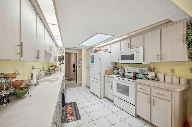 kitchen with white appliances, sink, a skylight, light brown cabinetry, and light tile patterned flooring