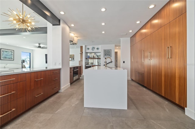 kitchen with ceiling fan with notable chandelier, a kitchen island with sink, wooden walls, sink, and pendant lighting