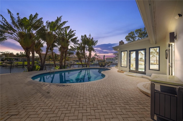 pool at dusk featuring a patio area and french doors