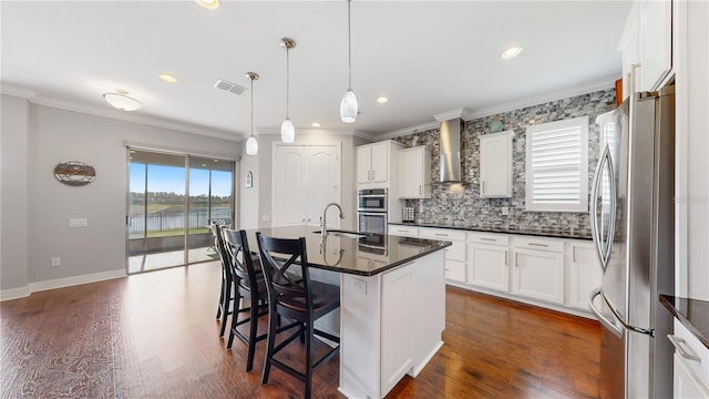 kitchen featuring a center island with sink, wall chimney range hood, a kitchen breakfast bar, stainless steel appliances, and white cabinets