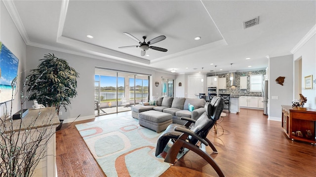 living room featuring a raised ceiling, wood-type flooring, and a healthy amount of sunlight