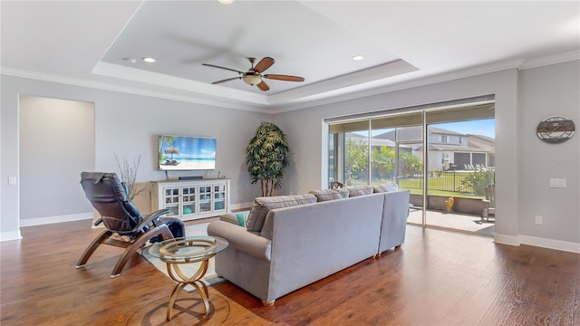 living room featuring a raised ceiling, wood-type flooring, crown molding, and ceiling fan