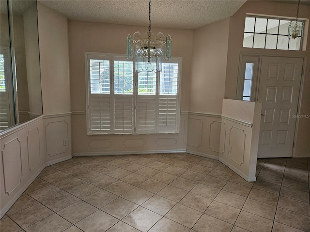 unfurnished dining area featuring light tile patterned flooring, a textured ceiling, and an inviting chandelier