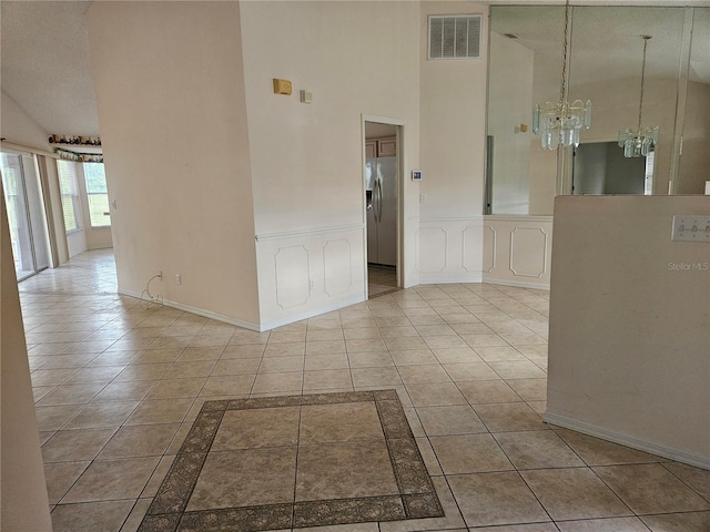 tiled empty room featuring a notable chandelier and high vaulted ceiling