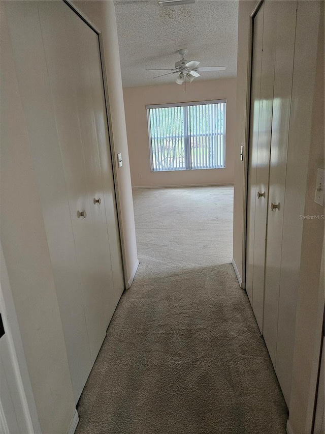 hallway with a textured ceiling and light colored carpet