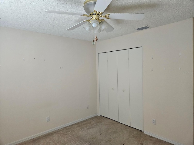 unfurnished bedroom featuring ceiling fan, a closet, light carpet, and a textured ceiling