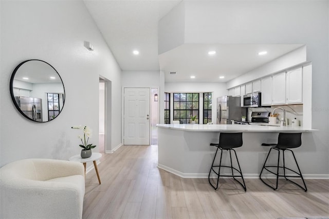 kitchen with a kitchen breakfast bar, kitchen peninsula, white cabinetry, and stainless steel appliances