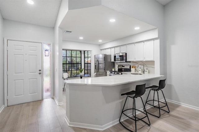 kitchen with white cabinets, sink, appliances with stainless steel finishes, kitchen peninsula, and a breakfast bar area