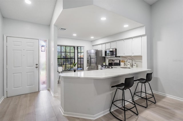 2582 Bentley Dr, Palm Harbor, FL 34684 - kitchen featuring stainless steel appliances, a peninsula, a sink, light wood-style floors, and white cabinetry