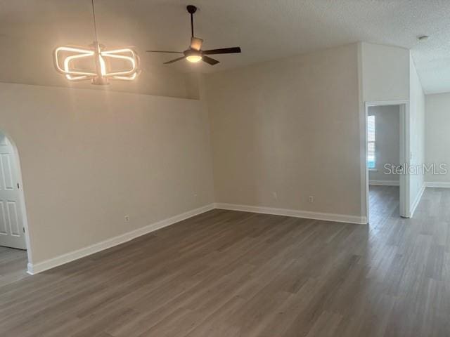 empty room featuring ceiling fan with notable chandelier, a textured ceiling, dark hardwood / wood-style flooring, and vaulted ceiling