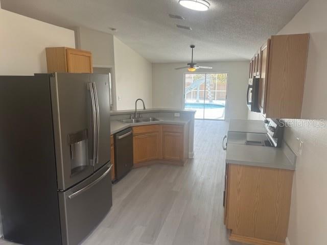 kitchen with kitchen peninsula, appliances with stainless steel finishes, a textured ceiling, sink, and light hardwood / wood-style floors