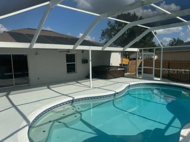 view of pool with a patio area, glass enclosure, and a hot tub