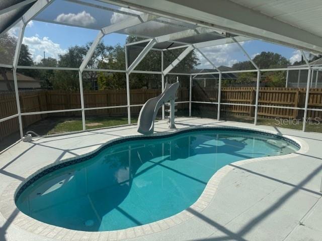 view of swimming pool with glass enclosure, a water slide, and a patio area