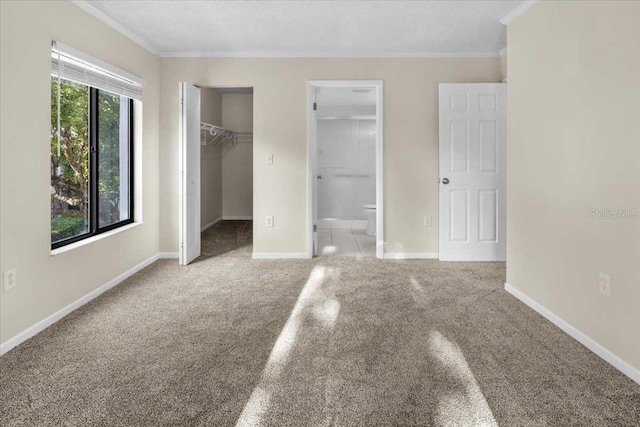 unfurnished bedroom featuring a textured ceiling, ornamental molding, light carpet, and connected bathroom