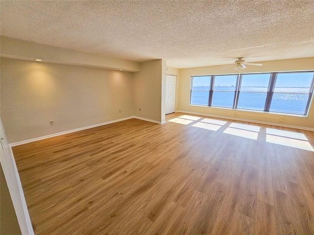 spare room with ceiling fan, a water view, light hardwood / wood-style floors, and a textured ceiling