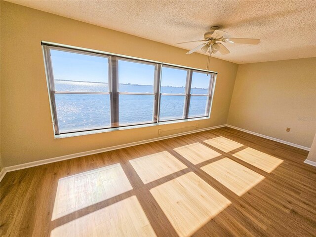 spare room featuring ceiling fan, a water view, wood-type flooring, and a textured ceiling