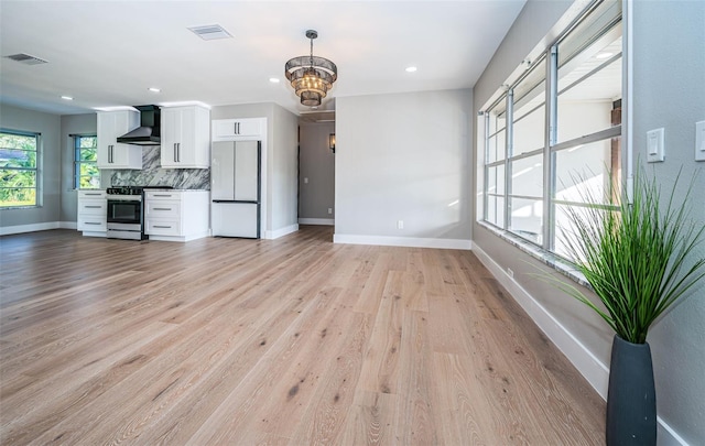 kitchen featuring white cabinetry, wall chimney exhaust hood, light hardwood / wood-style flooring, white refrigerator, and stainless steel stove