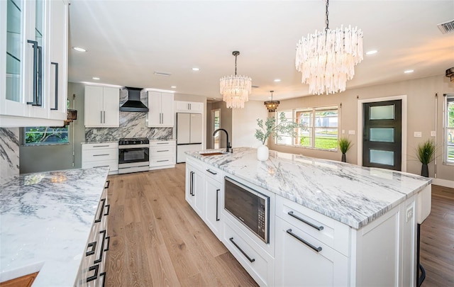 kitchen featuring gas stove, black microwave, a large island, wall chimney range hood, and white cabinets